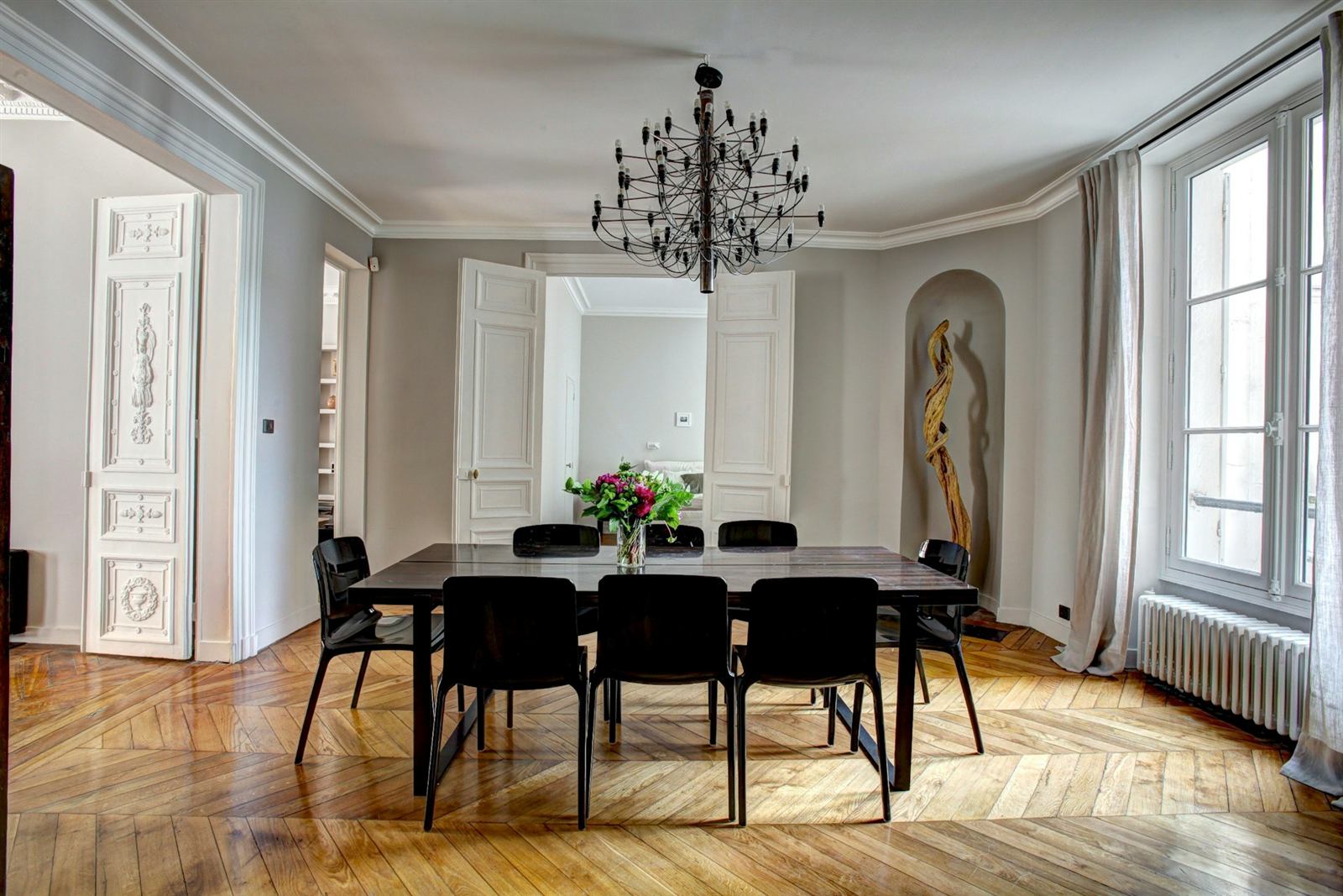 Salle à manger parisienne avec moulures, lustre, table noire et parquet
