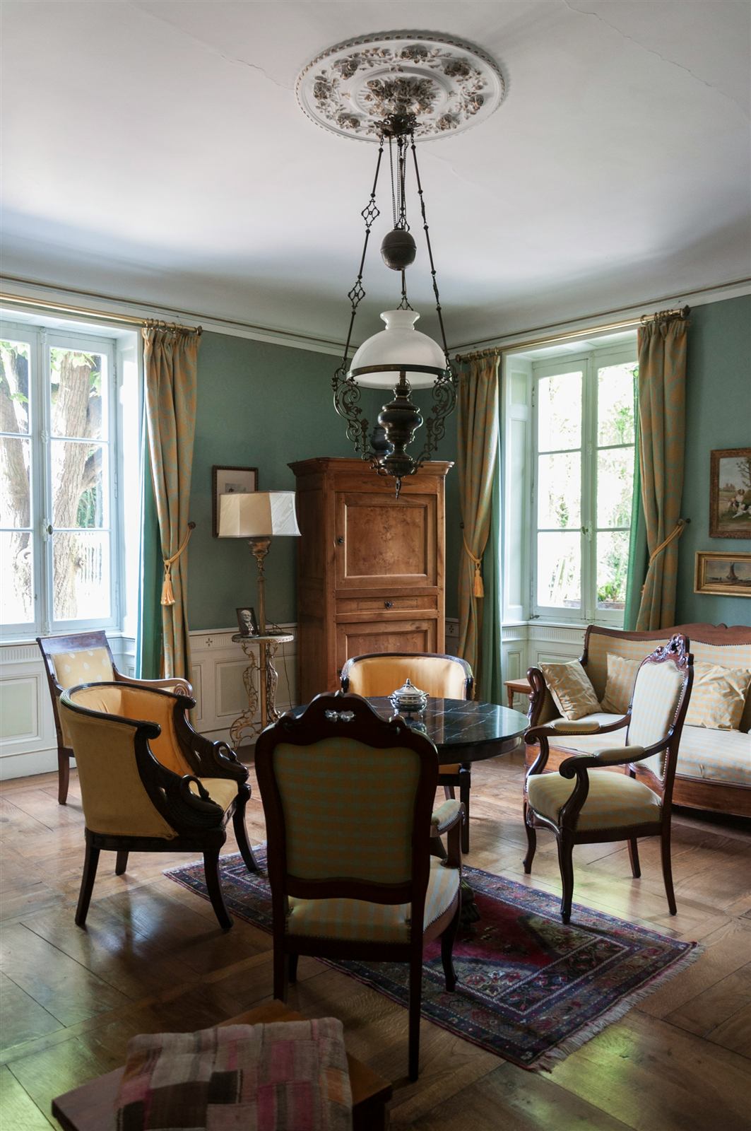 Salle à manger classique aux murs verts, lustre et fauteuils anciens